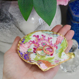 Hand holding a floral-patterned jewelry dish with rings inside, against a blurred background.