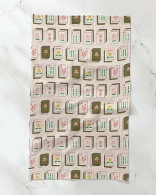 A rectangular kitchen towel with a repeating Mahjong tile pattern, laid flat on a white marble surface.