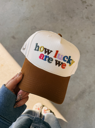 Cap with 'how lucky are we' text held by a person against a concrete background