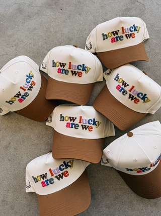 Collection of baseball caps with 'how lucky are we' text on a gray surface