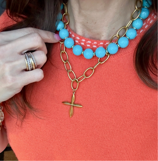Necklace with blue beads and gold chain worn by a person in an orange top.