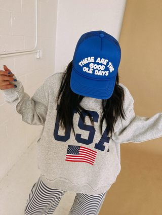 Person wearing a blue cap with text and a gray sweatshirt with 'USA' and an American flag.