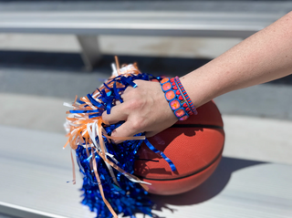 Hand holding a basketball with blue and orange pom-poms on a metal surface