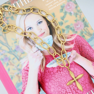 Woman holding a gold chain necklace with a magazine in the background