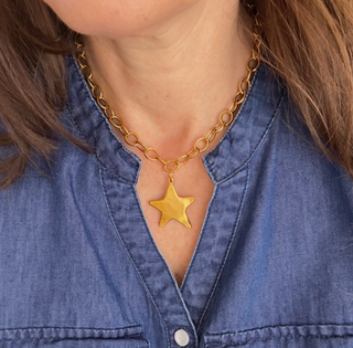 Gold necklace with a star pendant worn by a person in a blue denim shirt.