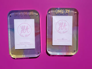 Two acrylic magnetic photo frames with custom text in gold metallic ink and monogram inserts, displayed side-by-side against a vibrant magenta background.