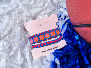 Set of colorful bracelets on a card with 'Spirit Bracelet Set' text, placed on blue tinsel and white shredded paper.